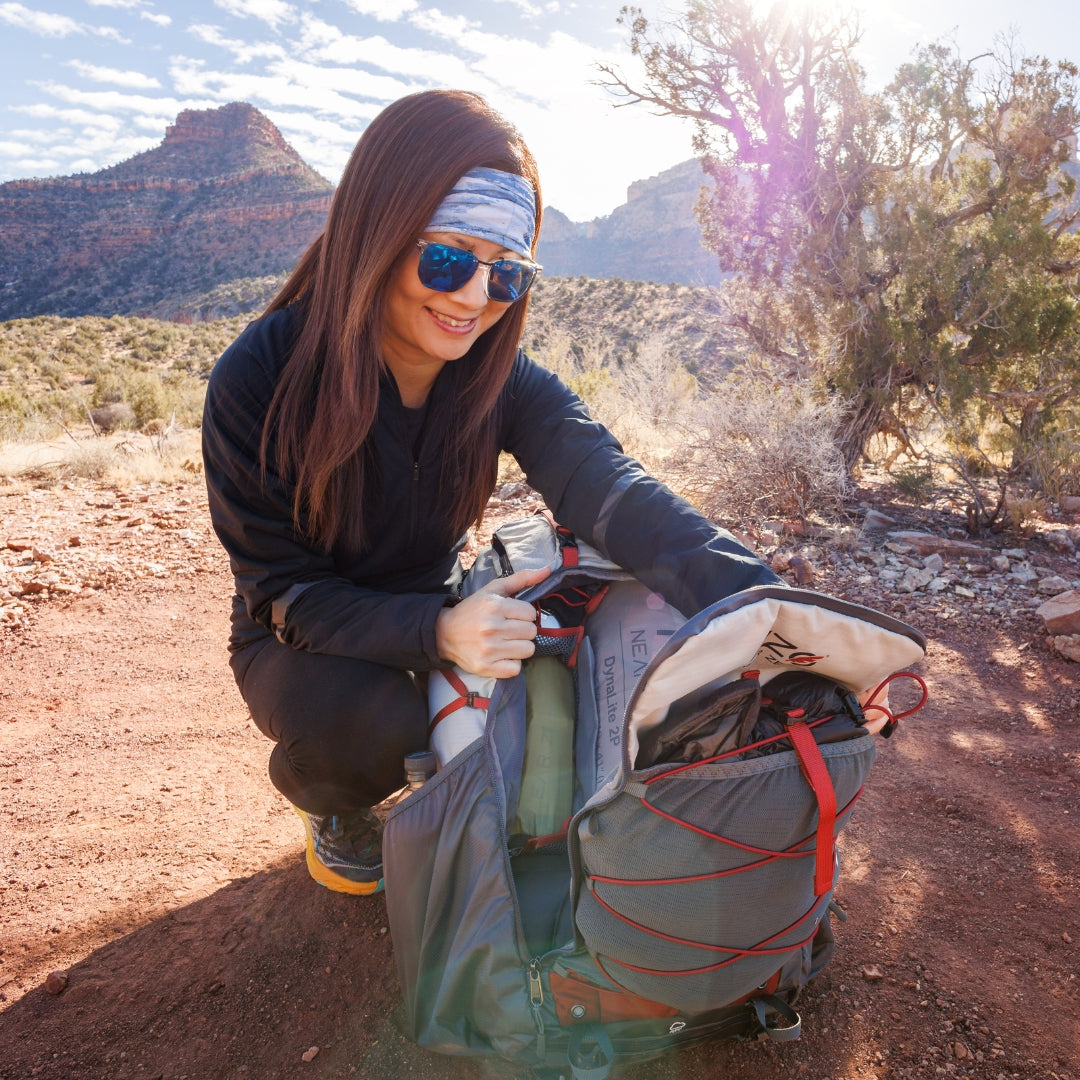 Near Zero Outdoor Gear - The Dean TR 50 Overnight Hiking Backpack - Woman reaching for things inside of backpack out in field