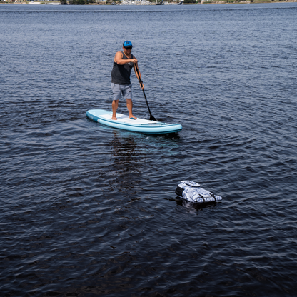 Dry Pocket - Waterproof Floating Backpack Dry Bag - Snow Camo - Floating in water in front of paddleboarder