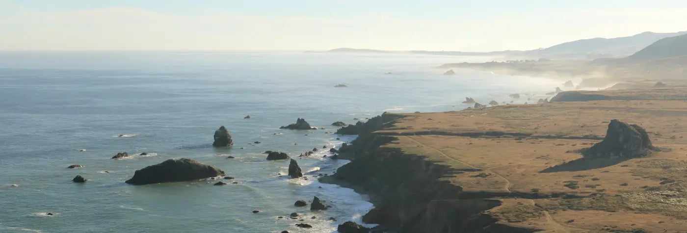 Coastal landscape with ocean, rocks, and grassy land.  (Toltrek banner image for Women's Apparel collection page).